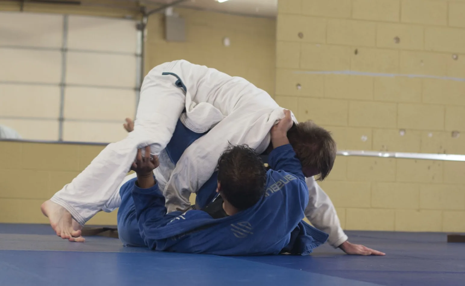 Deux pratiquants en kimono s'entraînant au sol dans un gymnase